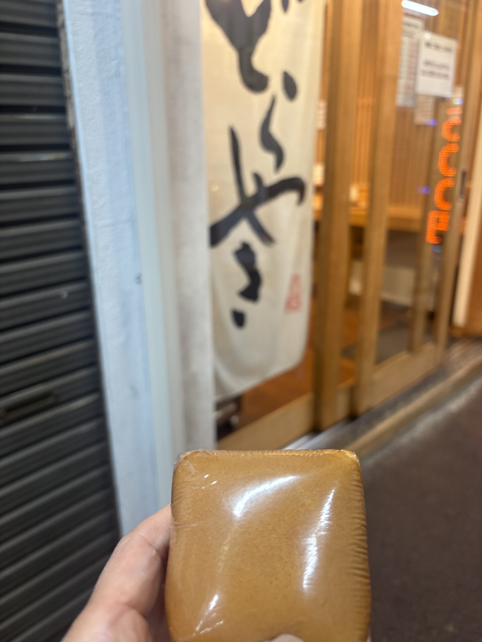 四角いどらやきを手に持つ・のれんのある店先